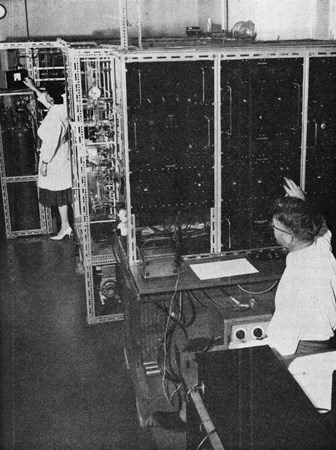 Miss A. Bermingham (Chemist) is working on the vacuum and chemical lines in the background, and Mr R. D. Carman (Physicist) is working on the iron shield surrounding proportional counter and electronic counting equipment in the foreground.