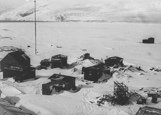 Buildings in a field of snow and surrounded by mountains.