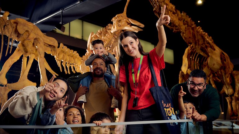 Children and carers in Dinosaur Walk exhibition with a museum staff member