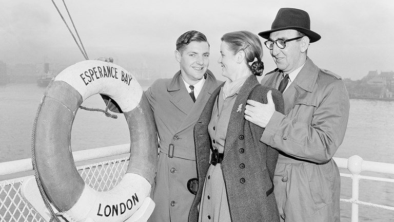 Two men and a woman (a son with his mother and father) standing in front of a white railing. To the left of the picture is a life preserver ring with the words “London / Esperance Bay” printed on it. 