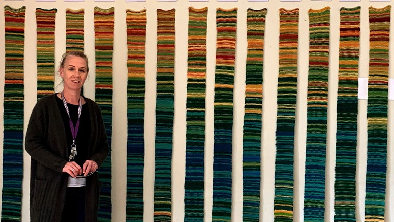 Woman standing front of an installation of narrow knitted strips