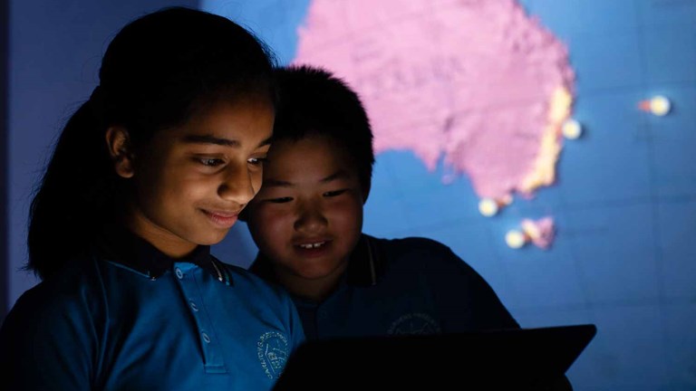 Two children looking a ipad. There is a large scale globe in background