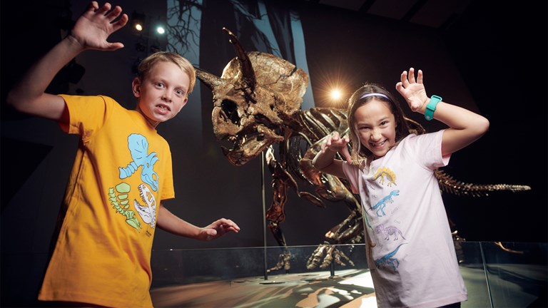 Children wearing dinosaur-print t-shirts pretend to roar, next to articulated Triceratops horridus skeleton on display in the Triceratops: Fate of the Dinosaurs exhibition in Melbourne Museum, during a media preview event.