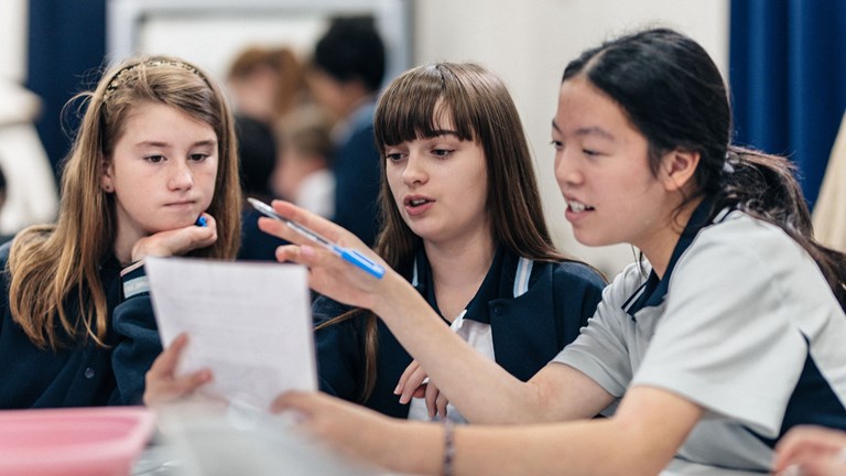 Three students in a classroom reading a document.