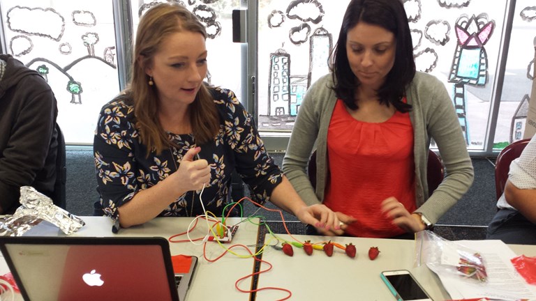 Two teachers sitting at a desk doing a STEM experiment with strawberries