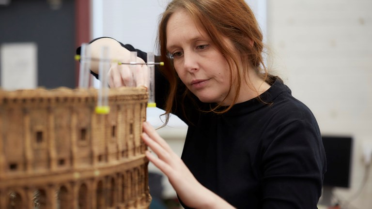 An auburn-haired woman works on a cork model of a Roman Colosseum