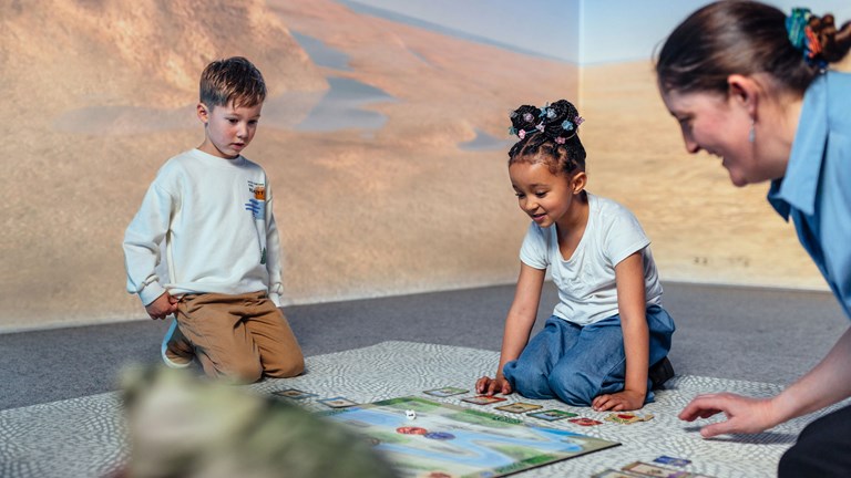 Two children and an adult playing a board game on the floor