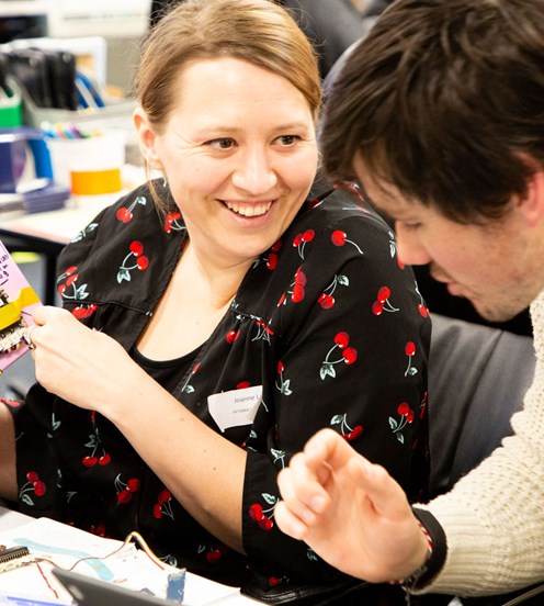 Two people sitting at a desk collaborating. There is a computer and other electronic components visible.