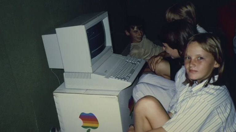 Teenage looking at the camera she is sitting in front of an early Apple Computer