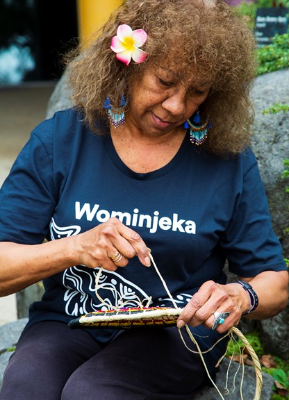 An Indigenous Elder weaving a basket from coloured grasses