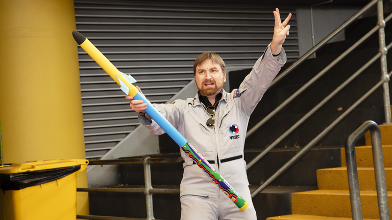 A person stands in the amphitheatre, counting down with one hand and holding a whistle rocket in the other.