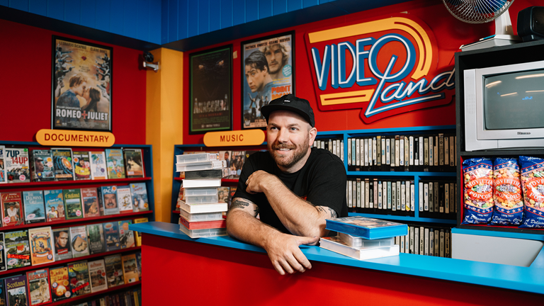 Callum Preston behind the counter of his replica 1990s video store, a place of significance during his carefree and joyous teenage years. 