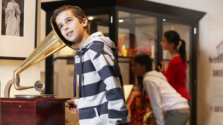 A student listens with their ear to the horn of a gramophone.