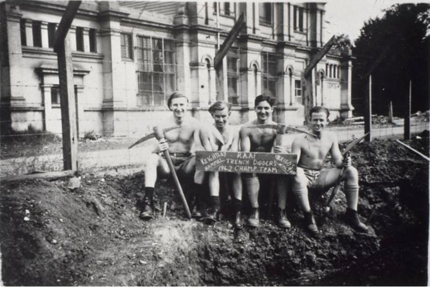 Shirtless soldiers sit in front of a trench. 