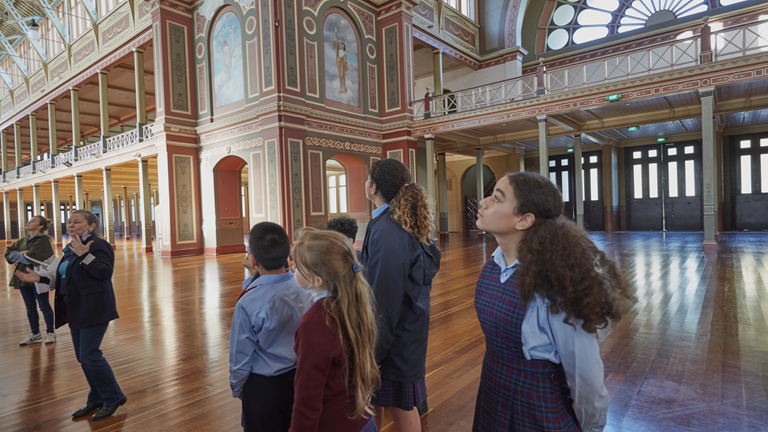 Students taking a tour of the Royal exhibition building, peering at the ornate wall moldings and painted frescos.