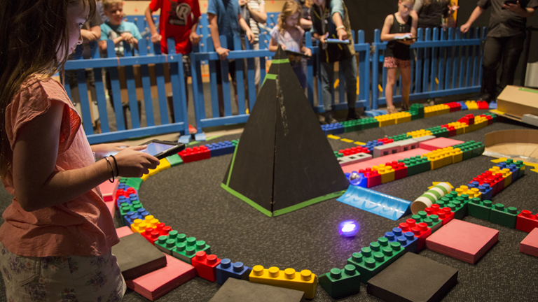 A child uses an iPad to guide a spherical robot around a maze.